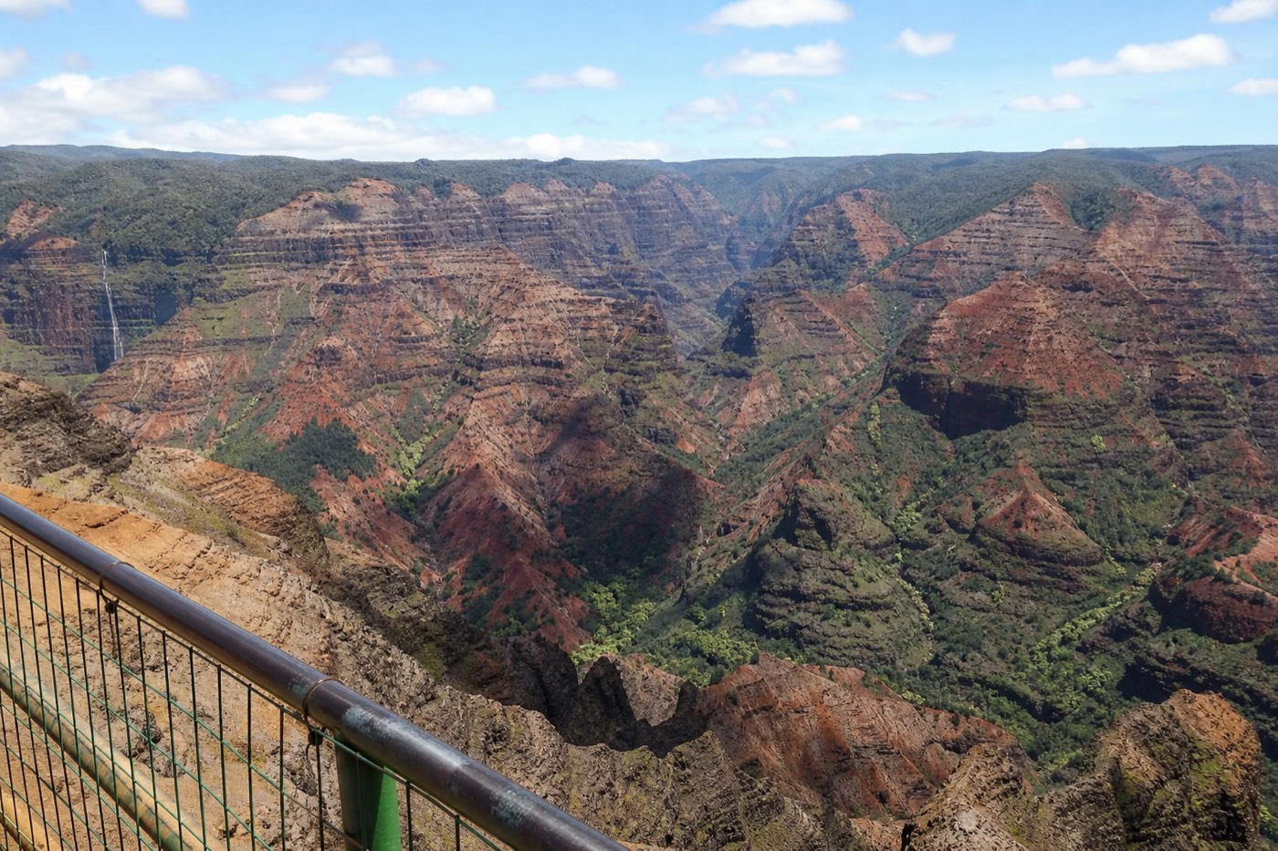 Layered red cliffs and green ridges seen from a Waimea Canyon lookout on Kauai