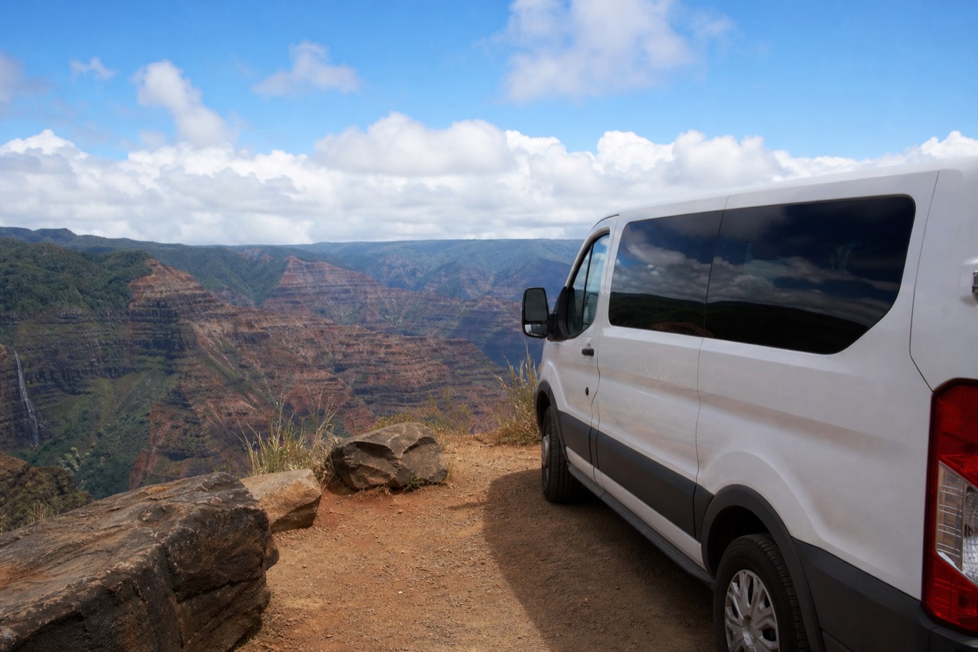 A small-group tour van at a Waimea Canyon lookout beside travelers who arrived in a rental car