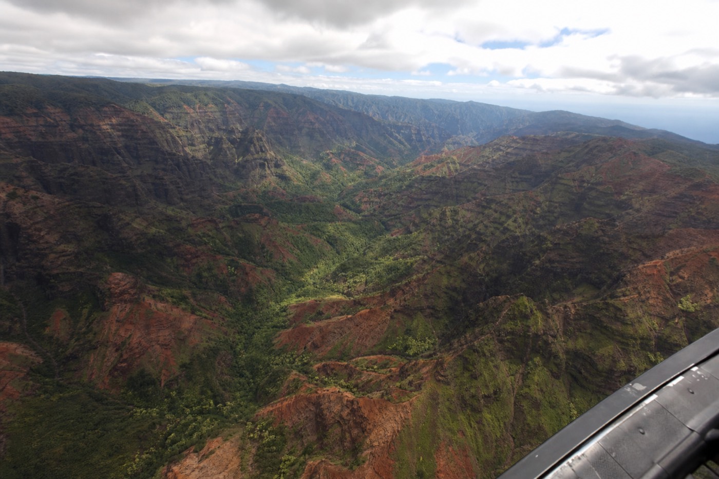 Passenger photographing Waimea Canyon from the open doorway of a doors-off helicopter over Kauai