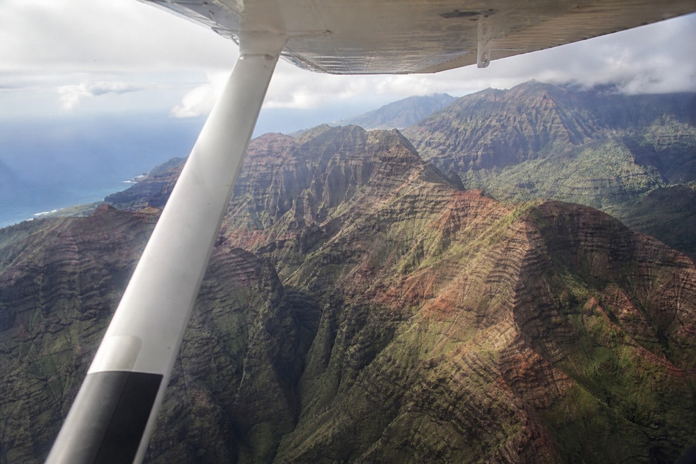 High-wing scenic airplane cruising above Waimea Canyon and the Nā Pali coastline on Kauai