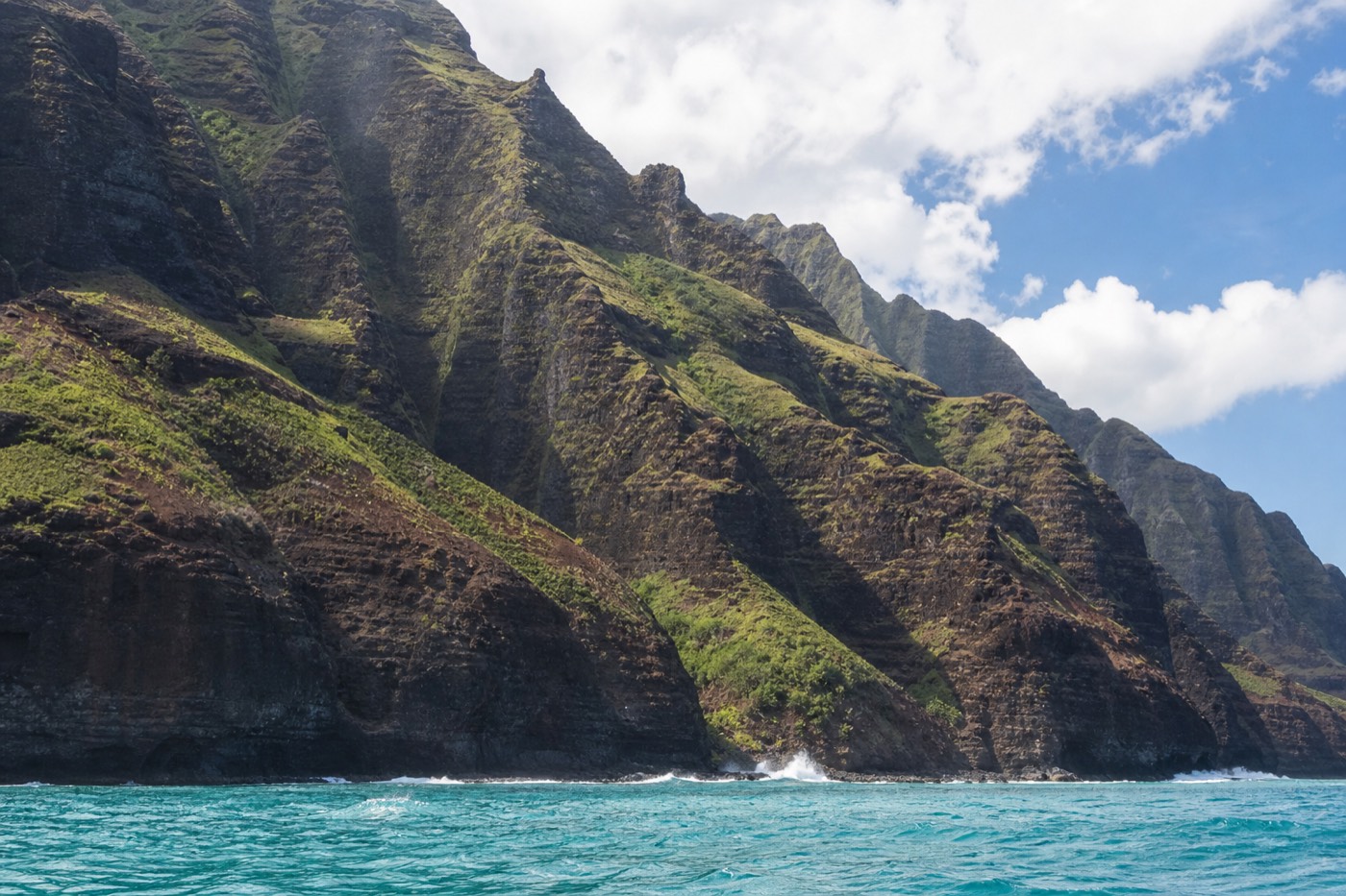 Split view of a catamaran below the Nā Pali cliffs and a helicopter flying over the same coastline