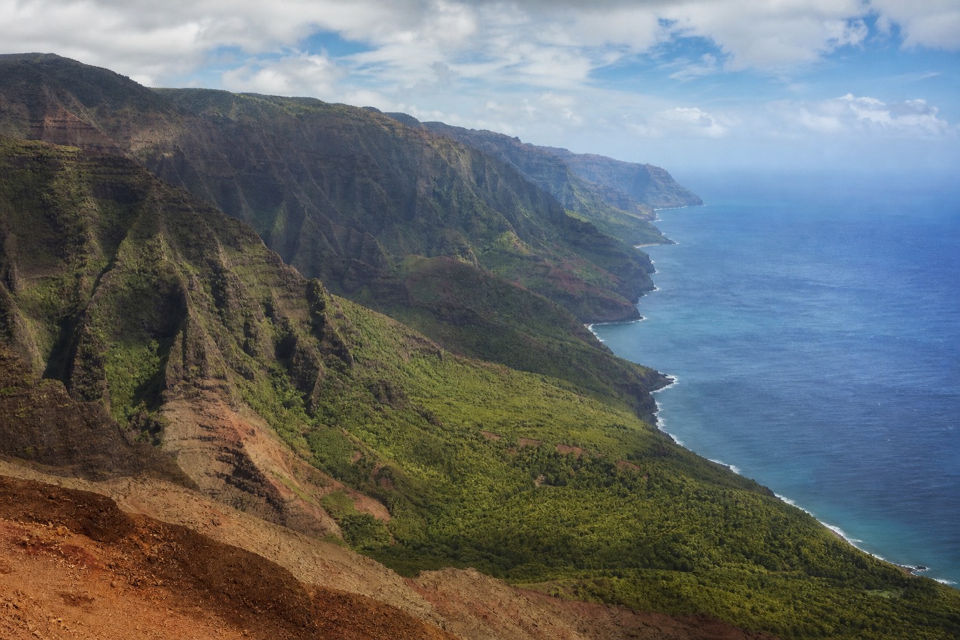 Waimea Canyon red cliffs at sunrise with the Nā Pali coastline and a boat on the ocean beyond